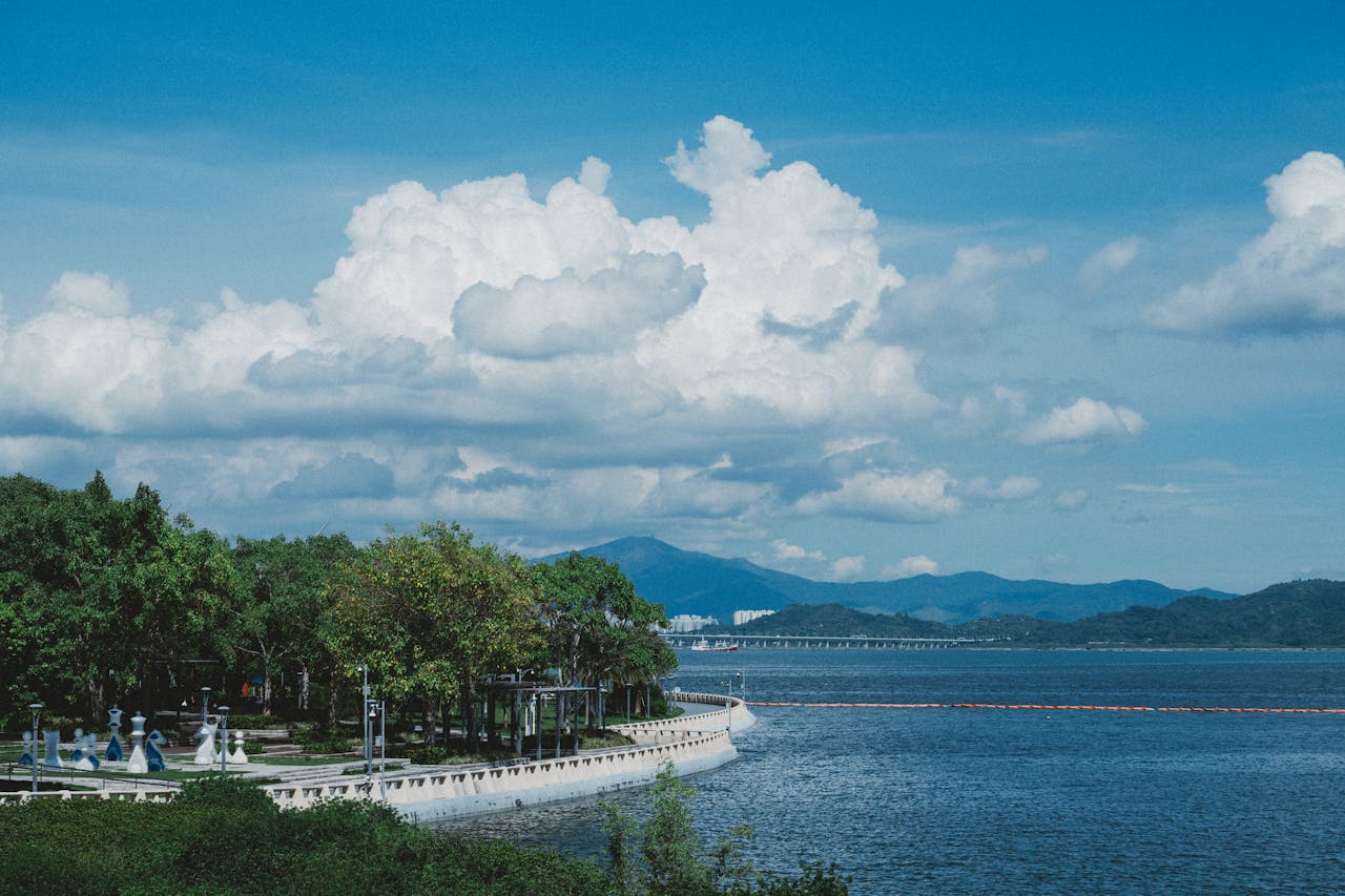 A scenic coastal landscape featuring lush greenery, a clear blue sky, and distant mountains over a tranquil body of water.